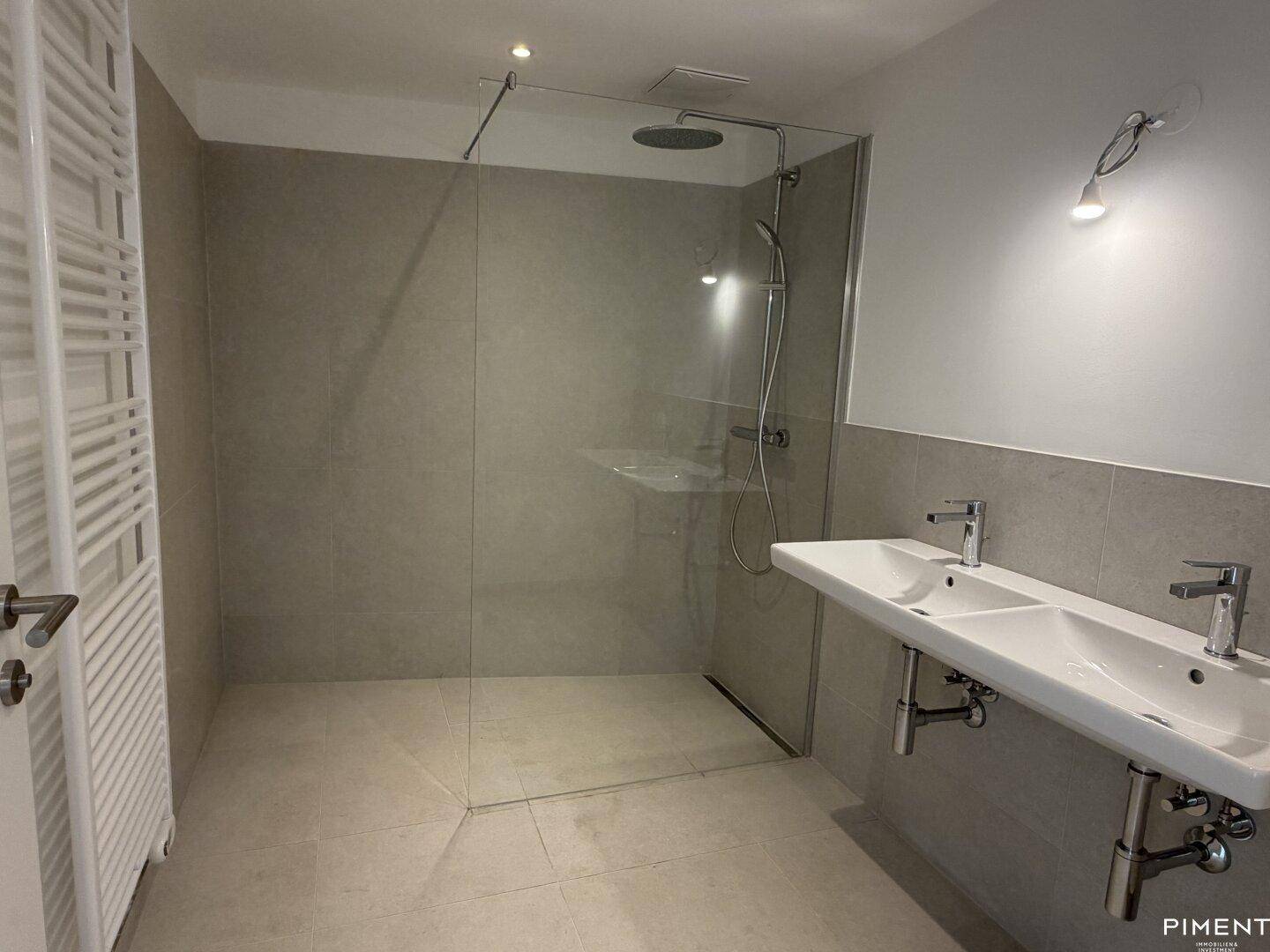 Modernes Badezimmer mit Doppelwaschbecken, großer begehbarer Dusche und Handtuchheizkörper.