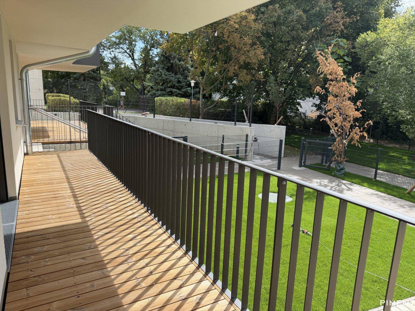 Langer Holzbalkon mit Metallgeländer und Blick ins Grüne, ideal für sonnige Stunden.