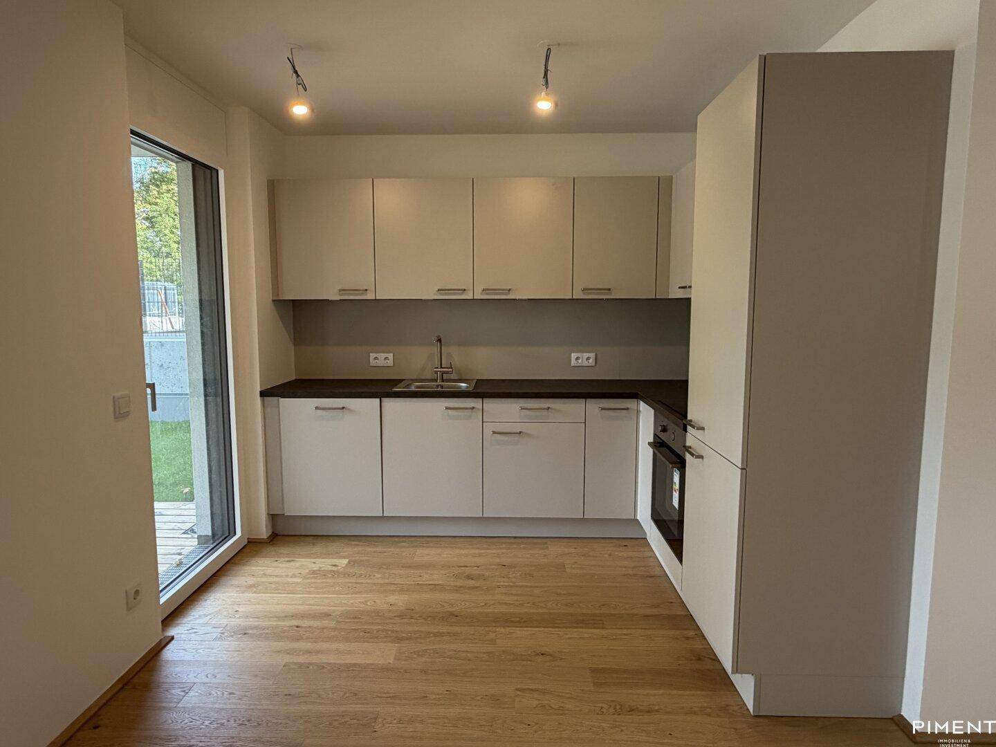 Moderne Einbauküche mit hellen Schränken, dunkler Arbeitsplatte und Zugang zum Garten.