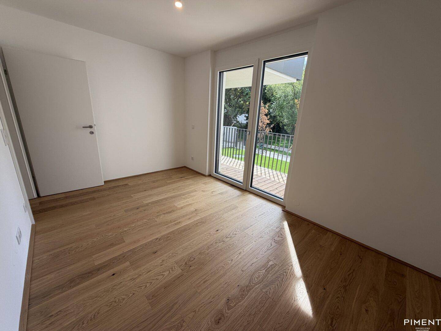 Lichtdurchflutetes Schlafzimmer mit Holzboden und Zugang zu einem Balkon, bietet eine angenehme Atmosphäre.