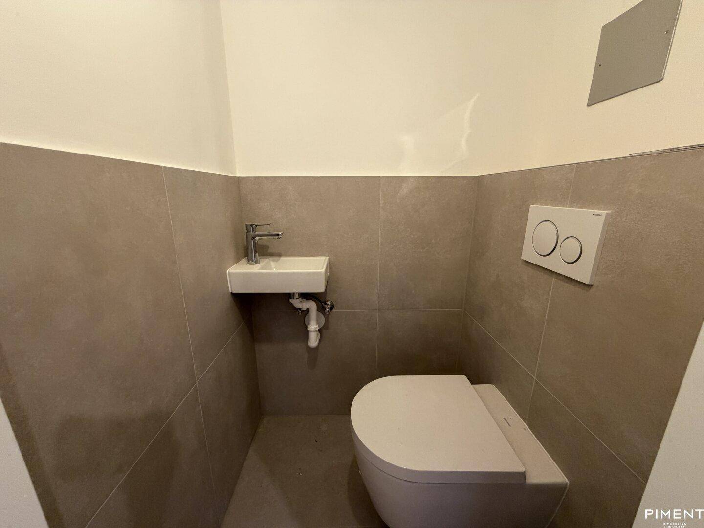 Separates Gäste-WC mit Wand-WC und kleinem Handwaschbecken, modern gefliest.