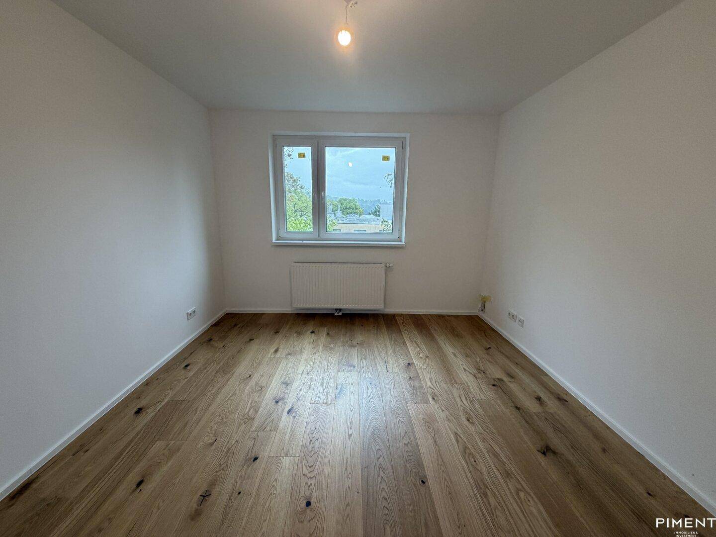 Leeres Schlafzimmer mit hellem Holzparkettboden und einem Fenster mit Ausblick.