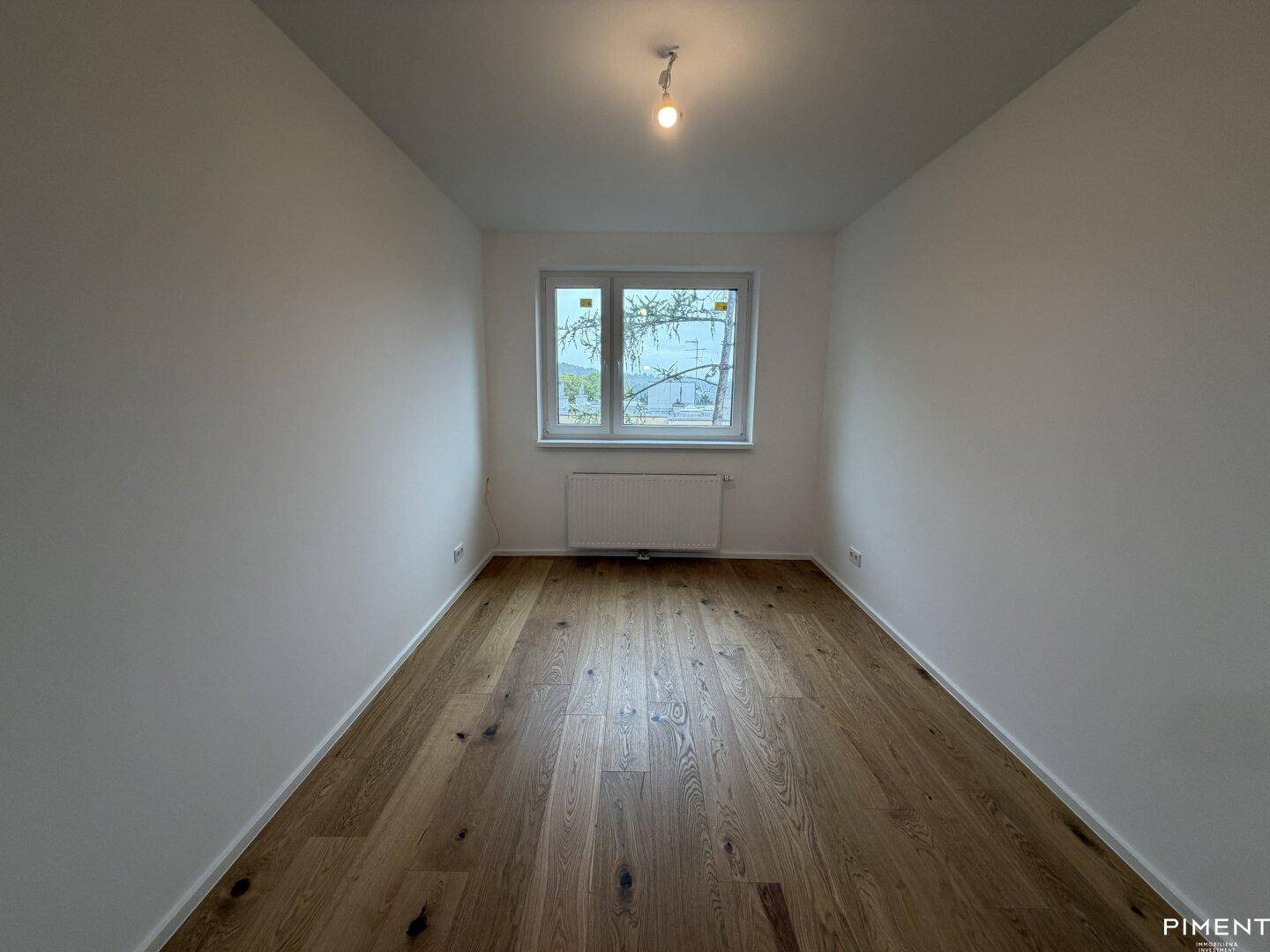 Weiteres leeres Schlafzimmer mit Holzparkett und einem Fenster für natürliches Licht.