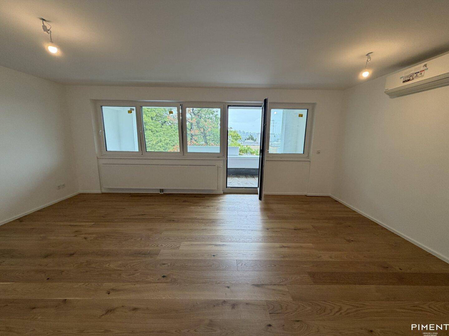 Lichtdurchflutetes Wohnzimmer mit Holzparkett, Klimaanlage und Zugang zum Außenbereich.