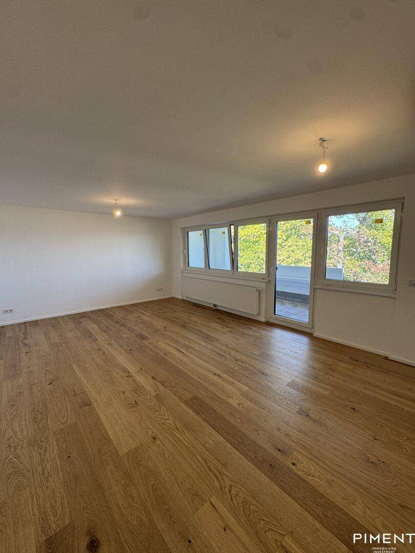 Helles, leeres Wohnzimmer mit neuem Holzparkettboden und Zugang zu einem Balkon.