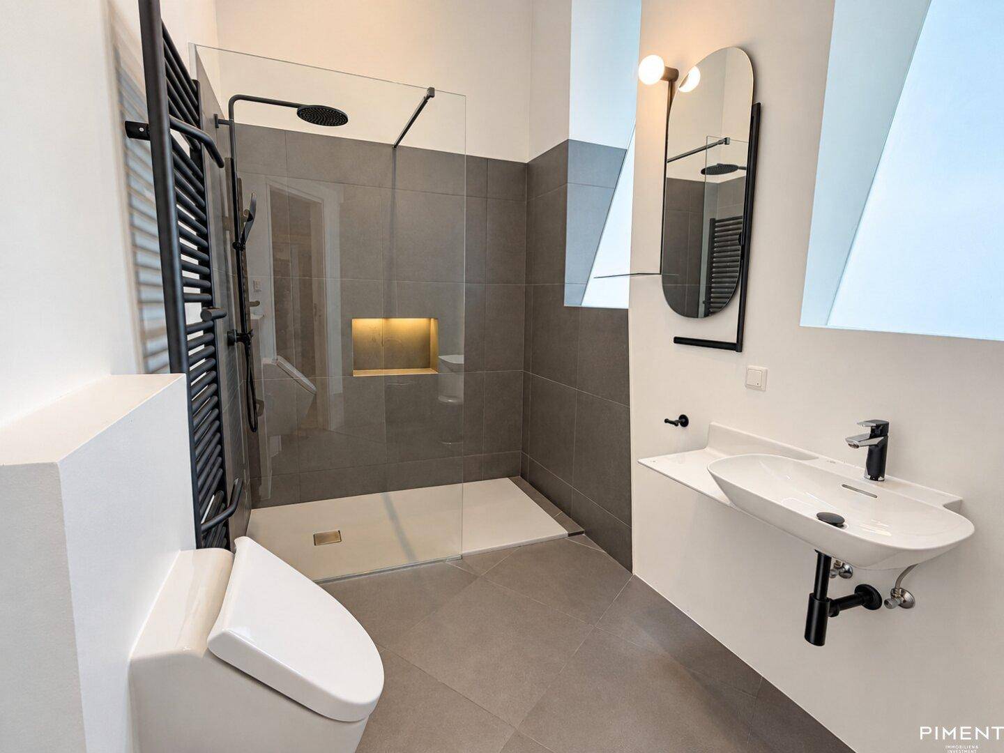 Modernes Badezimmer mit begehbarer Dusche, grauen Fliesen und Wand-WC.