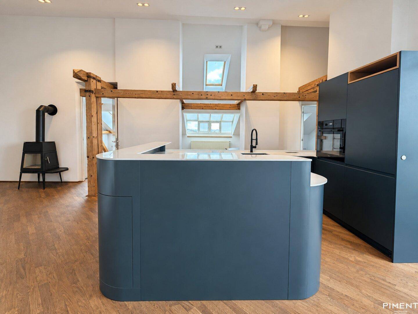Moderne Küche mit dunkelblauen Schränken, Kücheninsel und freiliegenden Holzbalken.