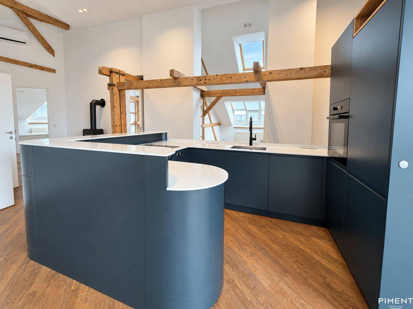 Moderne Küche mit dunkelblauen Schränken, Kücheninsel und freiliegenden Holzbalken.
