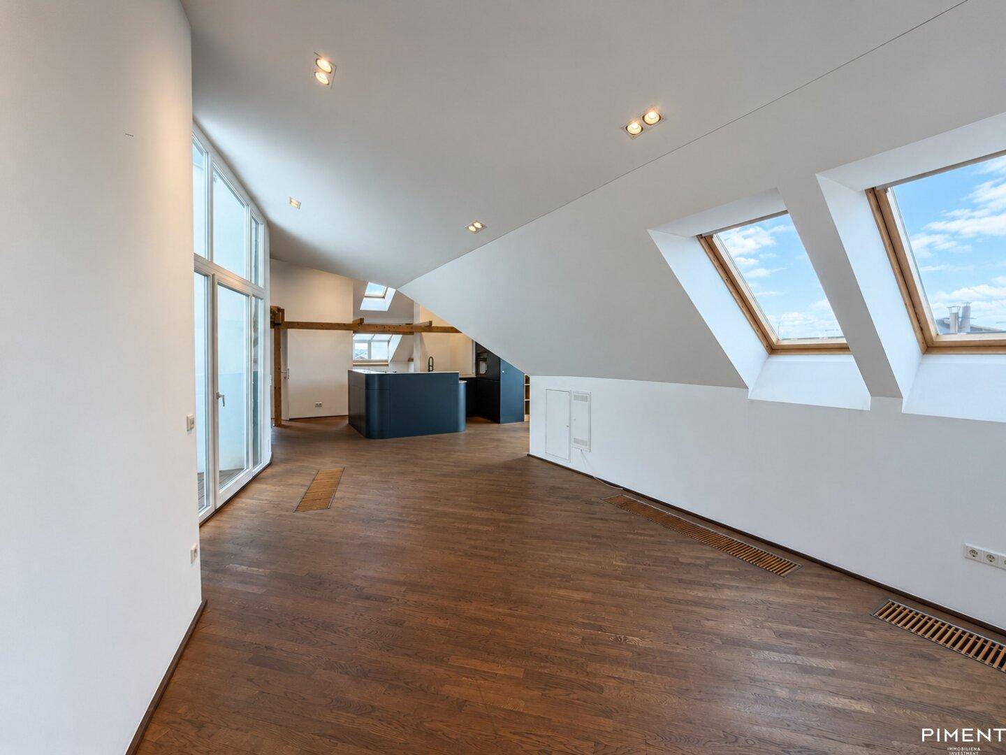 Offener Wohnbereich im Dachgeschoss mit Holzboden, großen Fenstern und Blick auf die Küche.