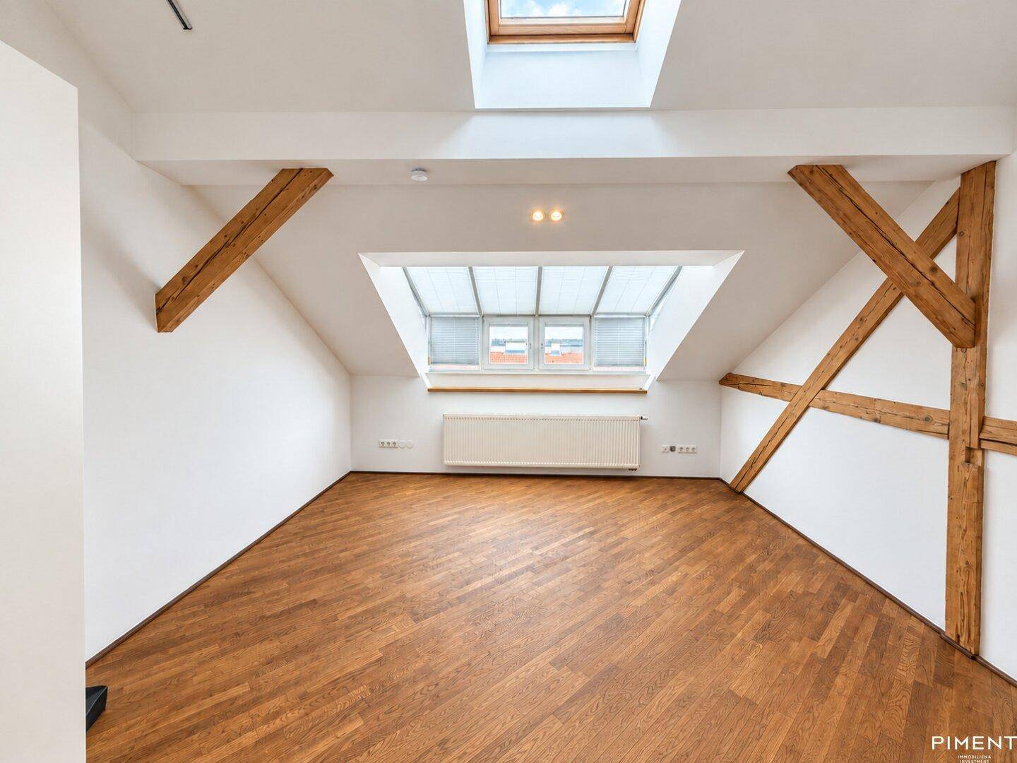 Geräumiger Dachbodenraum mit Holzbalken, Dachfenstern und dunklem Parkettboden.