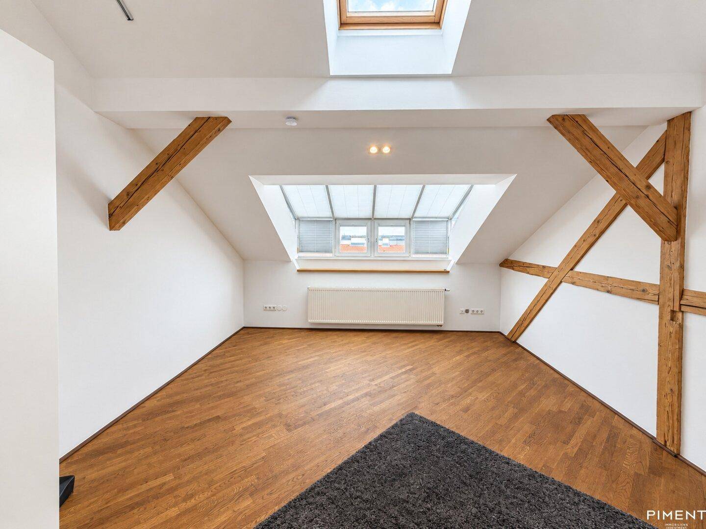 Geräumiger Dachbodenraum mit Holzbalken, Dachfenstern und dunklem Parkettboden.