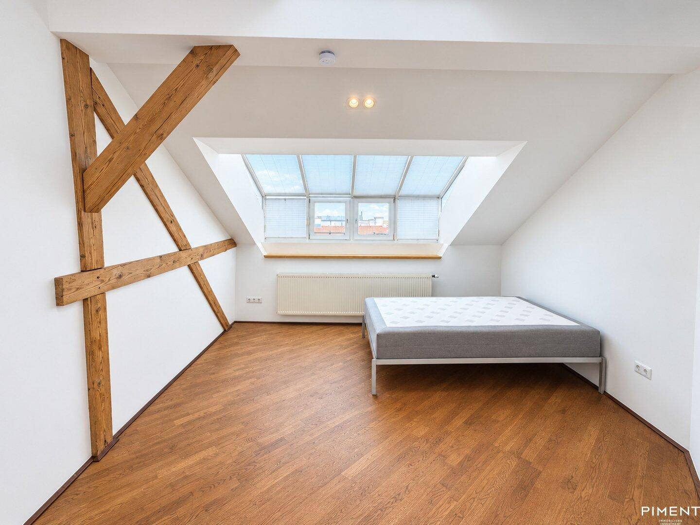 Schlafzimmer im Dachgeschoss mit Holzbalken, Dachfenstern und einem Bett.