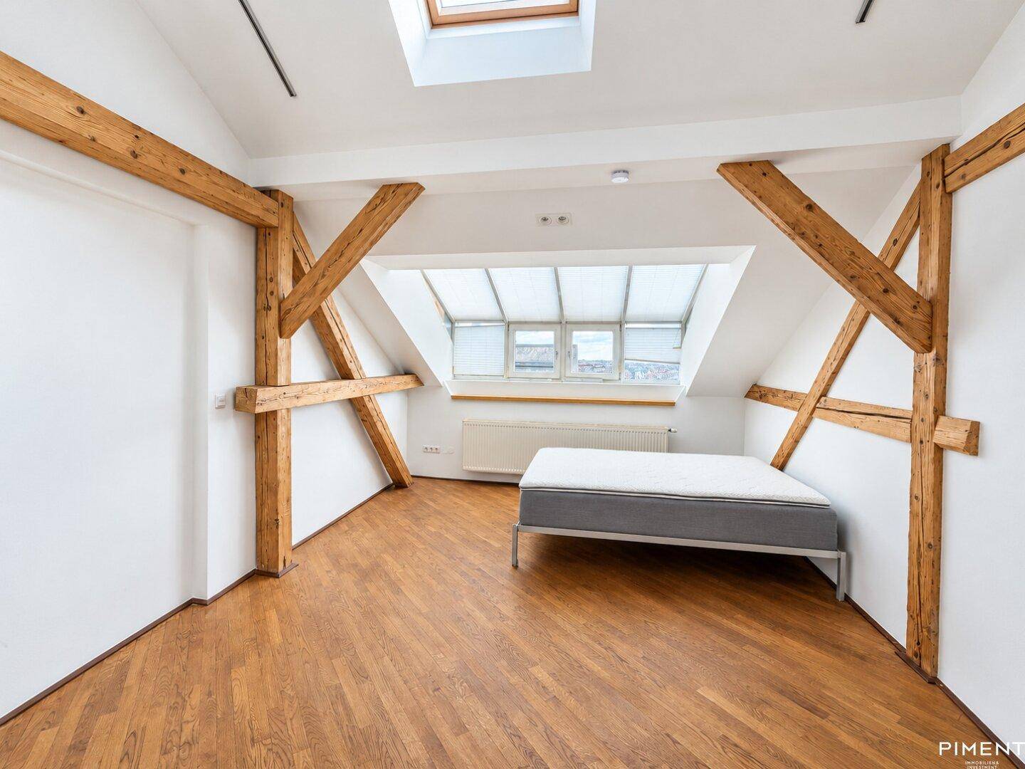 Schlafzimmer im Dachgeschoss mit Holzbalken, Dachfenstern und einem Bett.