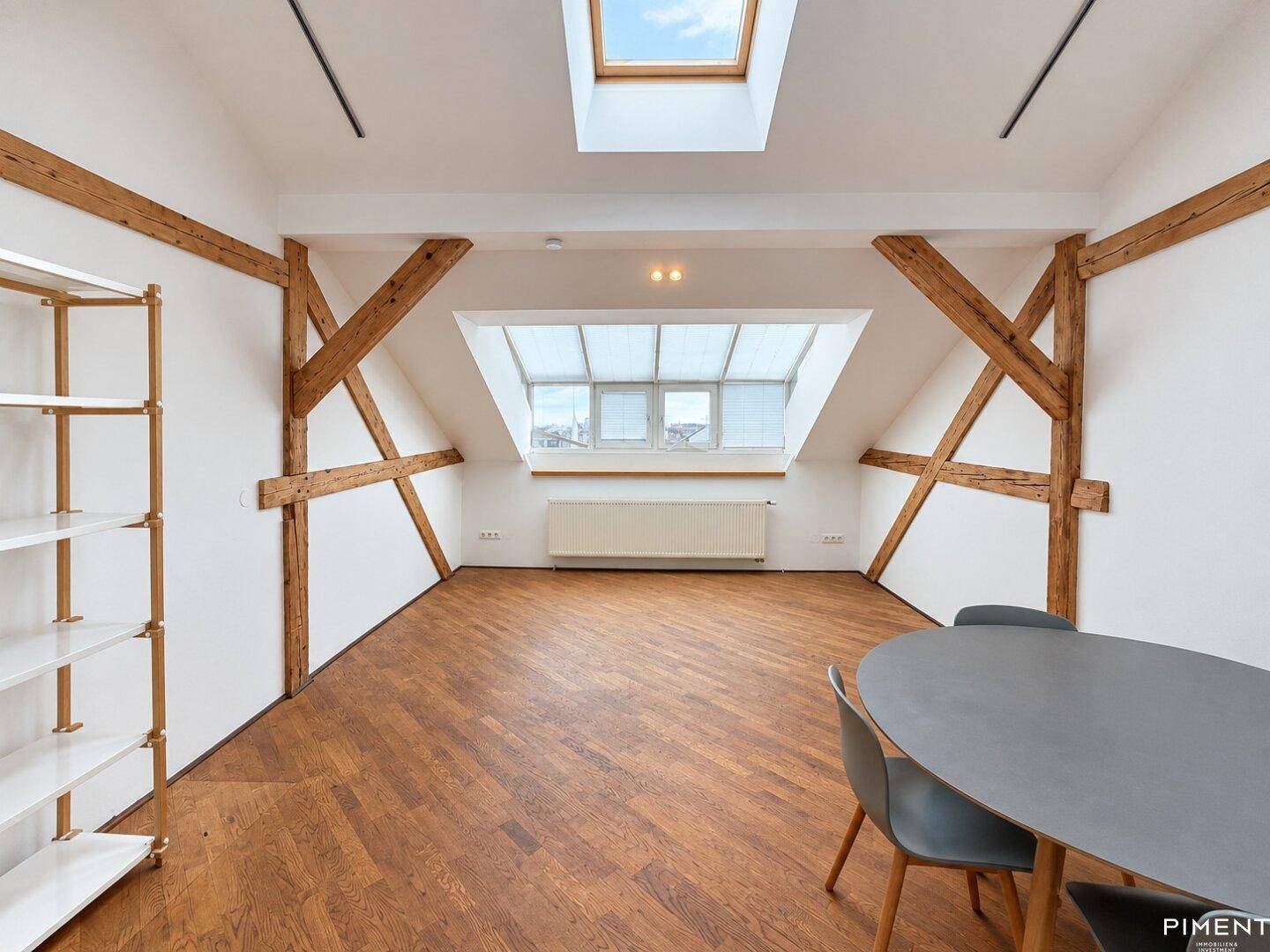 Dachbodenraum mit Holzbalken, Dachfenster, Regal und Esstisch.