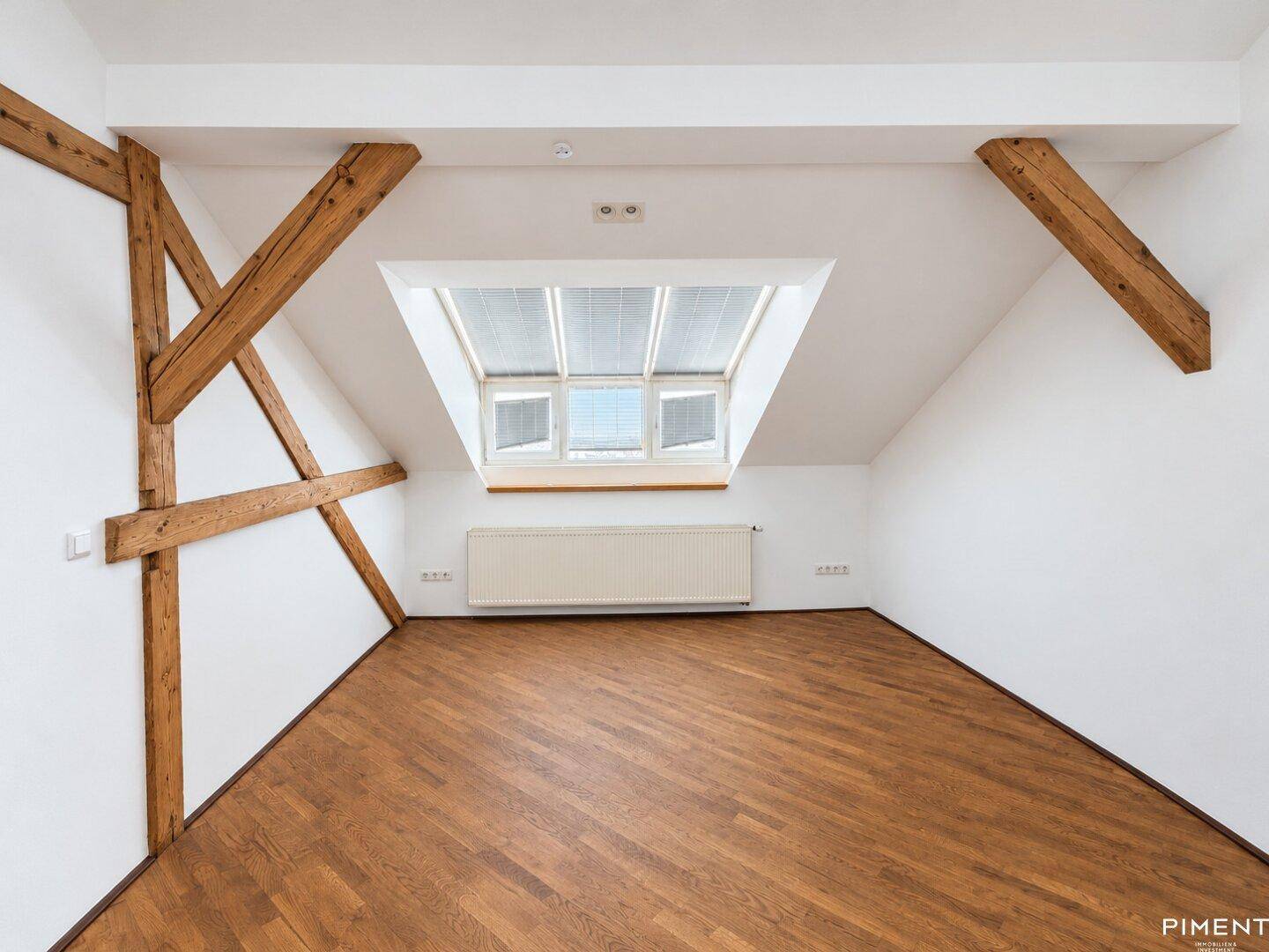 Dachbodenraum mit Holzbalken, Dachfenster und hellem Parkettboden.