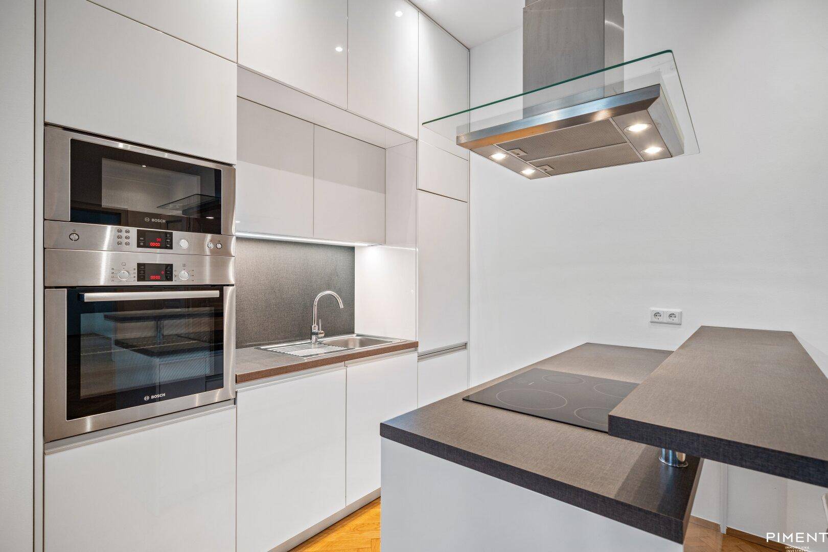 Moderne Einbauküche mit weißen Hochglanzfronten, Induktionskochfeld und integrierten Geräten.
