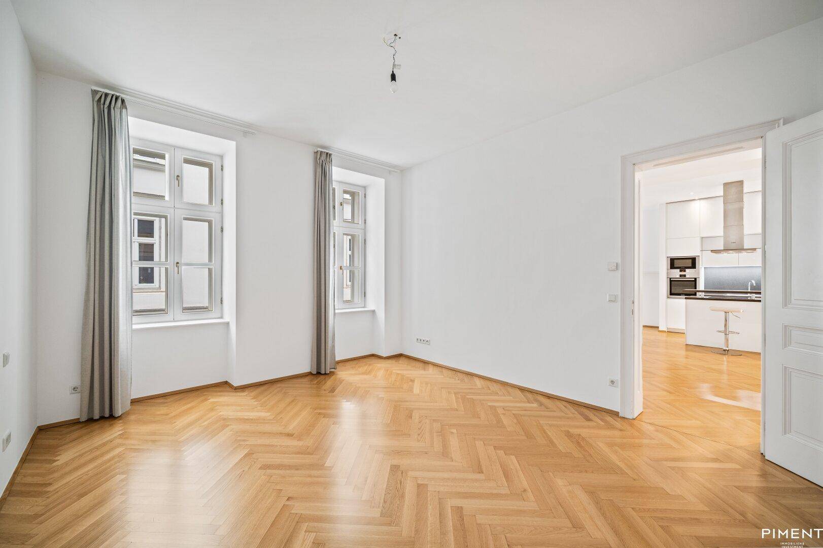 Helles Wohnzimmer mit Fischgrätparkett und Blick auf die moderne offene Küche.
