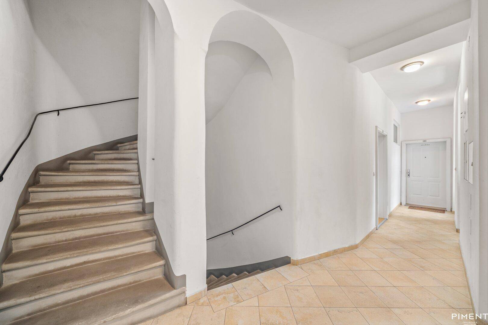 Geräumiger Treppenhausflur mit gefliestem Boden und geschwungener Steintreppe.
