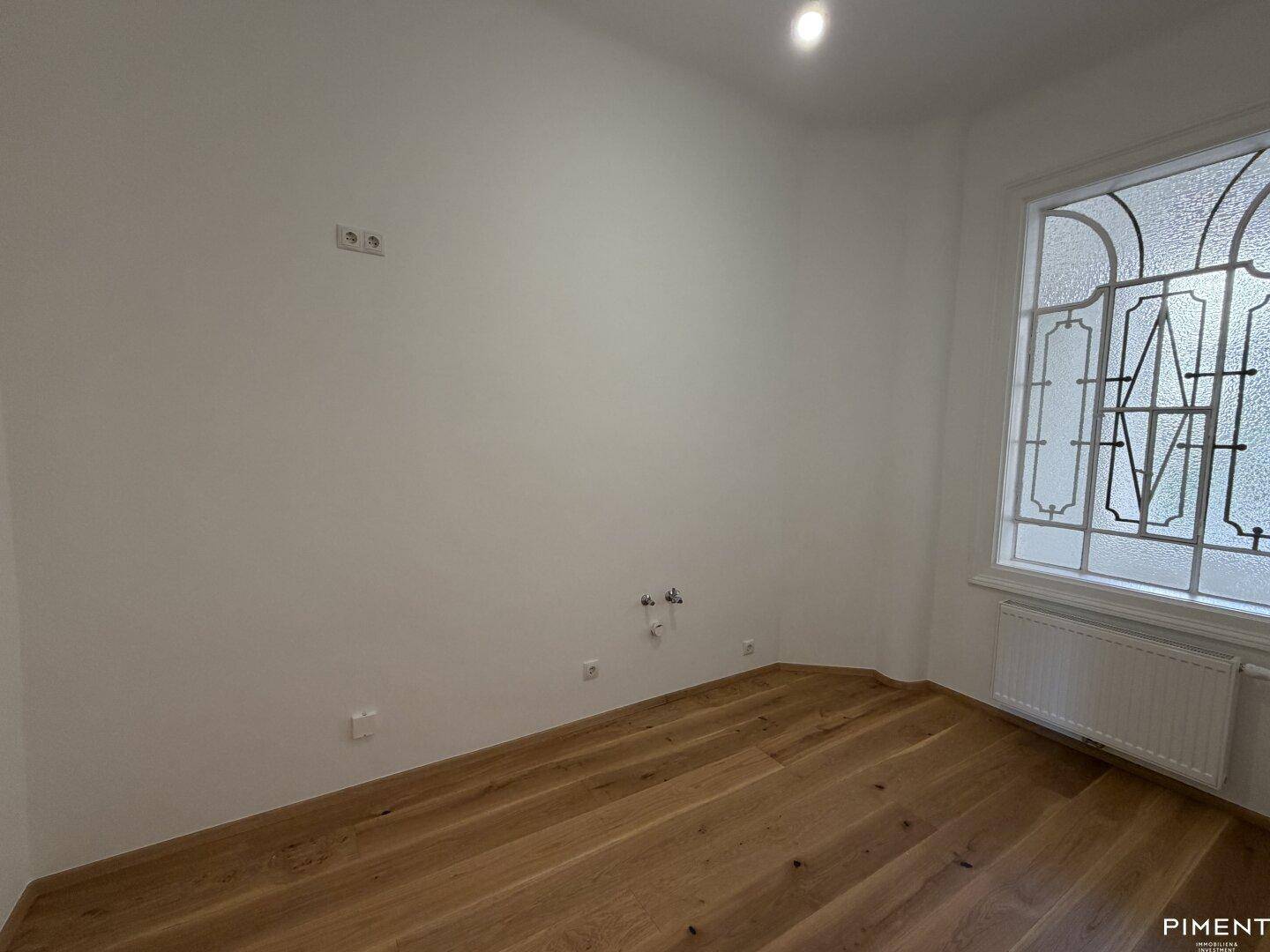 Kleinerer Raum mit Holzboden und einem Fenster mit dekorativem Gitter, ideal als Arbeitszimmer.
