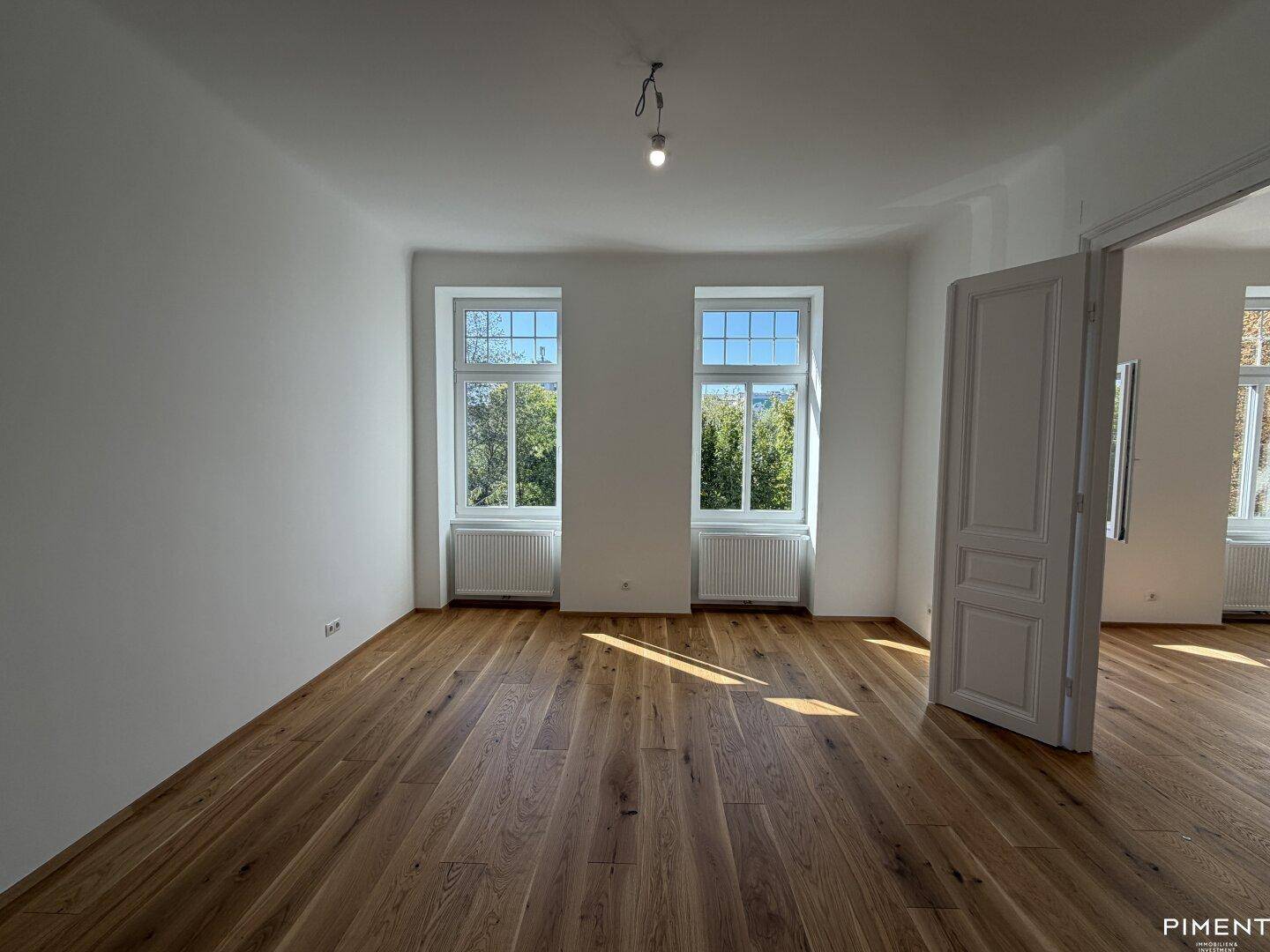 Lichtdurchfluteter Raum mit frisch verlegtem Parkettboden und hohen Fenstern, die viel Tageslicht hereinlassen.