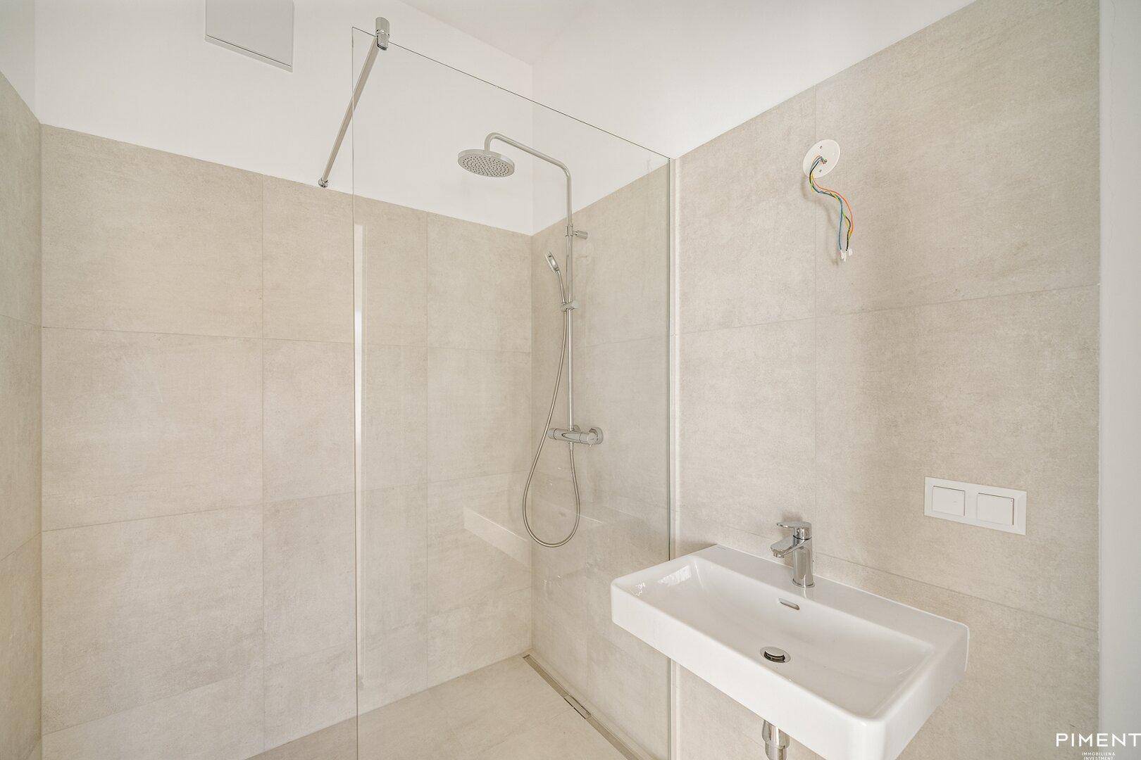 Modernes Badezimmer mit begehbarer Dusche, hellem Fliesenboden und einem einzelnen Waschbecken.