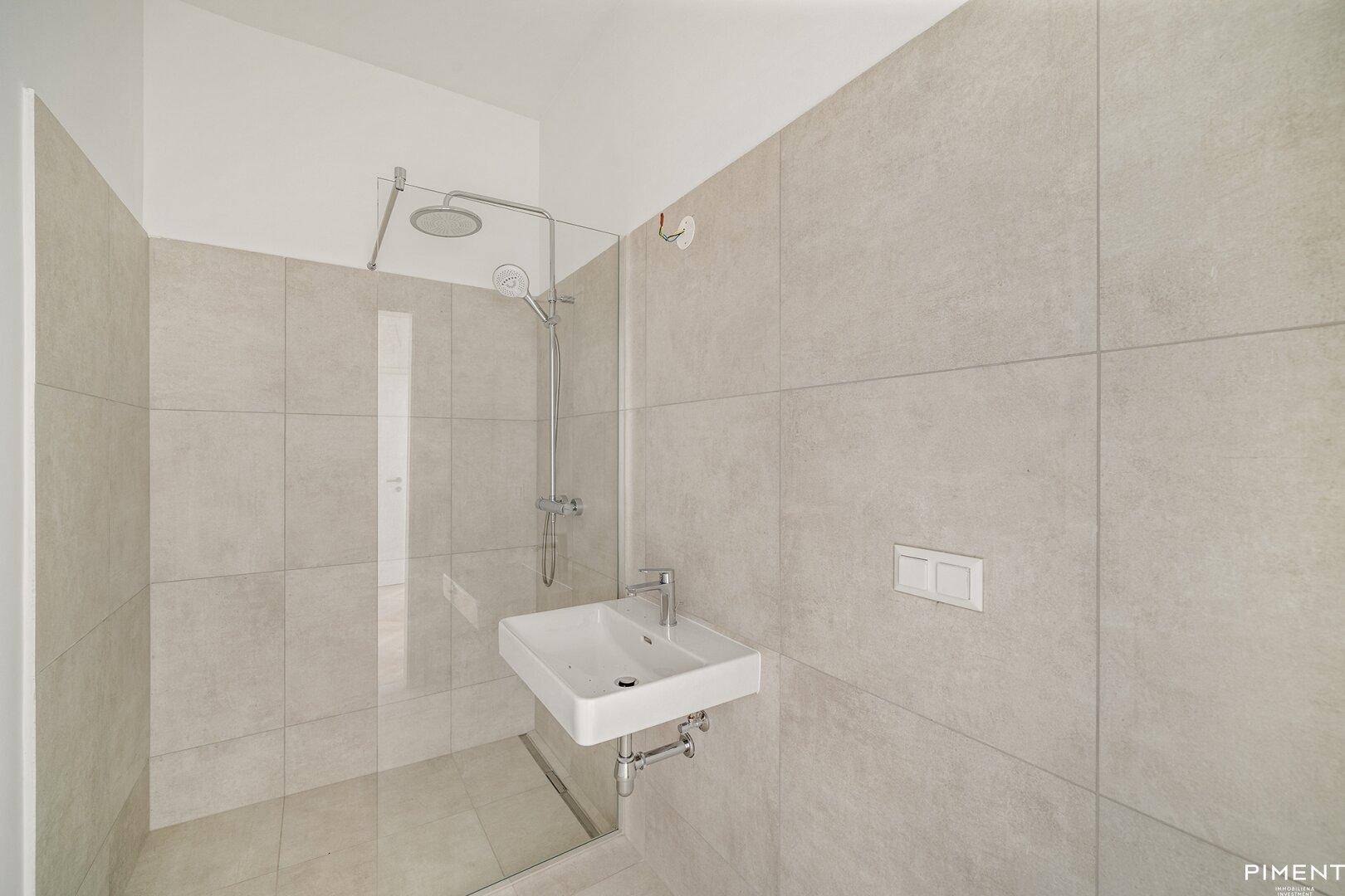 Modernes Badezimmer mit begehbarer Dusche, Regenduschkopf und hellen Fliesen an Wänden und Boden.