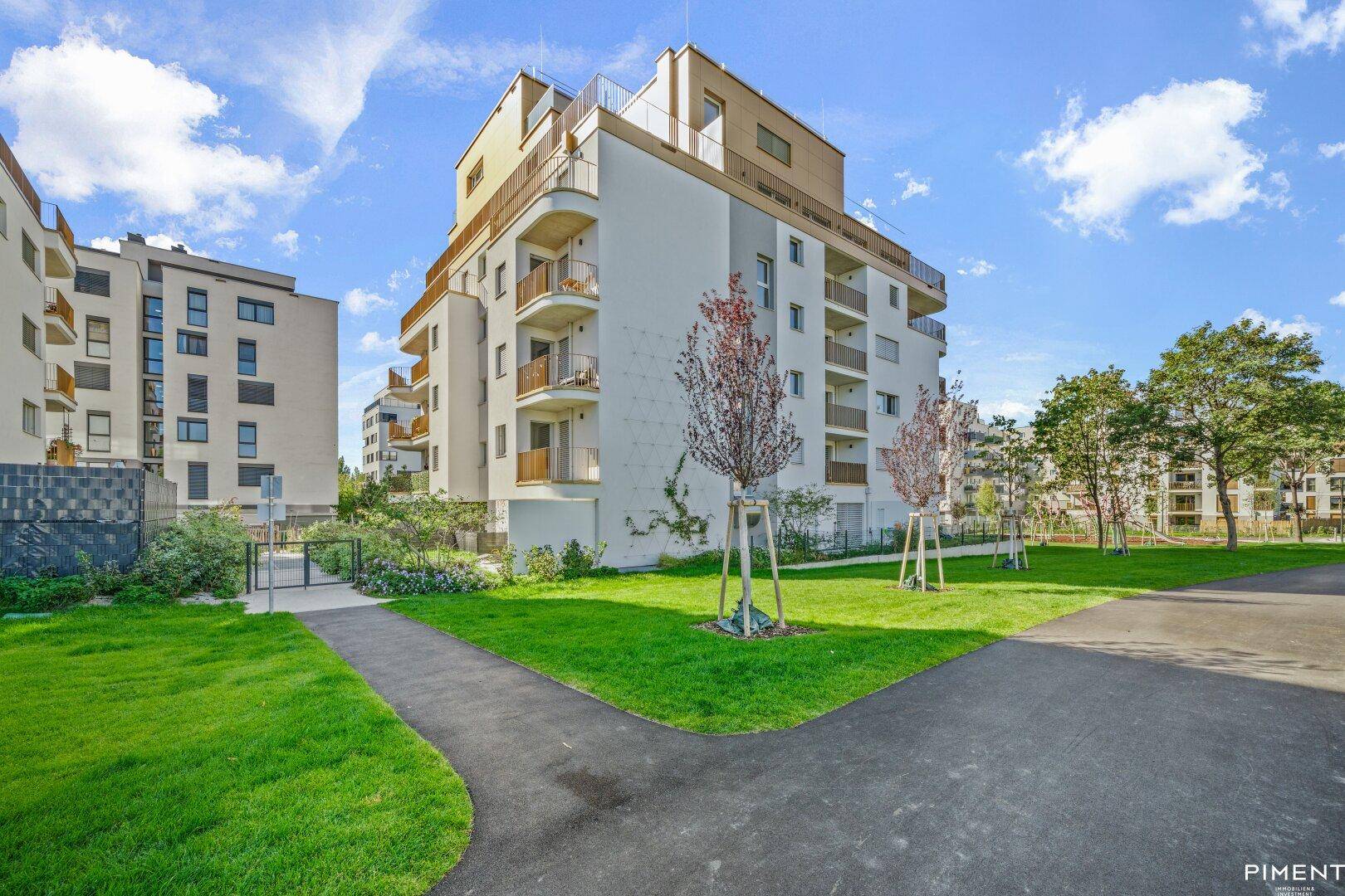 Ansicht eines modernen Wohnkomplexes mit weißer Fassade, Balkonen und jungen Bäumen auf der grünen Rasenfläche.