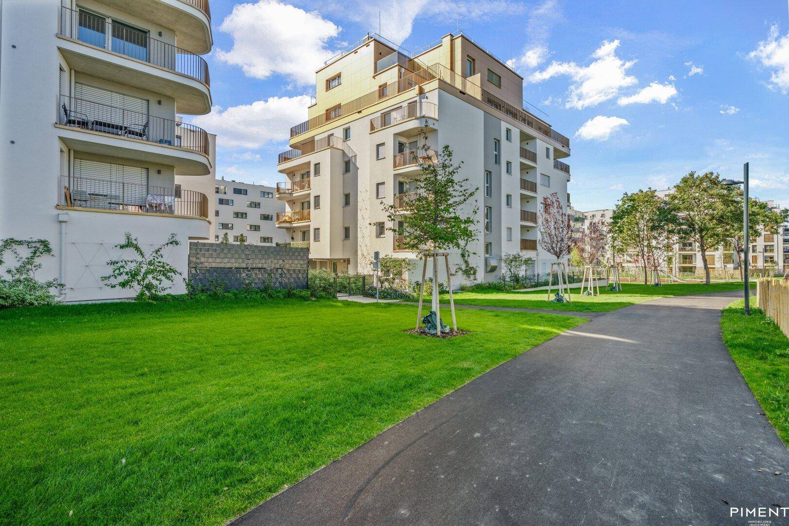 Moderne Wohnanlage mit weißer Fassade, Balkonen und weitläufigen Grünflächen mit jungen Bäumen.