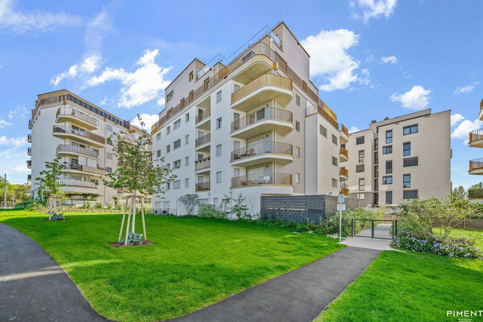 Moderne Wohngebäude mit weißen Fassaden und Balkonen, umgeben von gepflegten Grünflächen und Gehwegen.