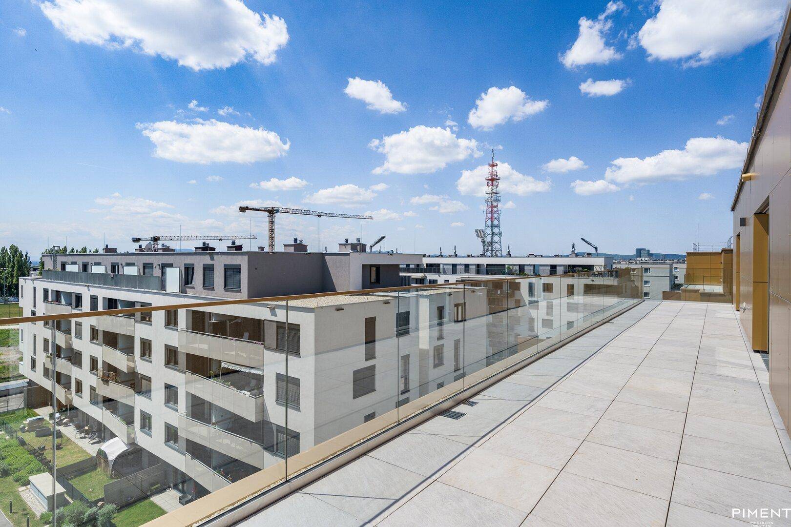 Geräumige Dachterrasse mit Glasgeländer und weitem Blick über moderne Gebäude und die Umgebung.