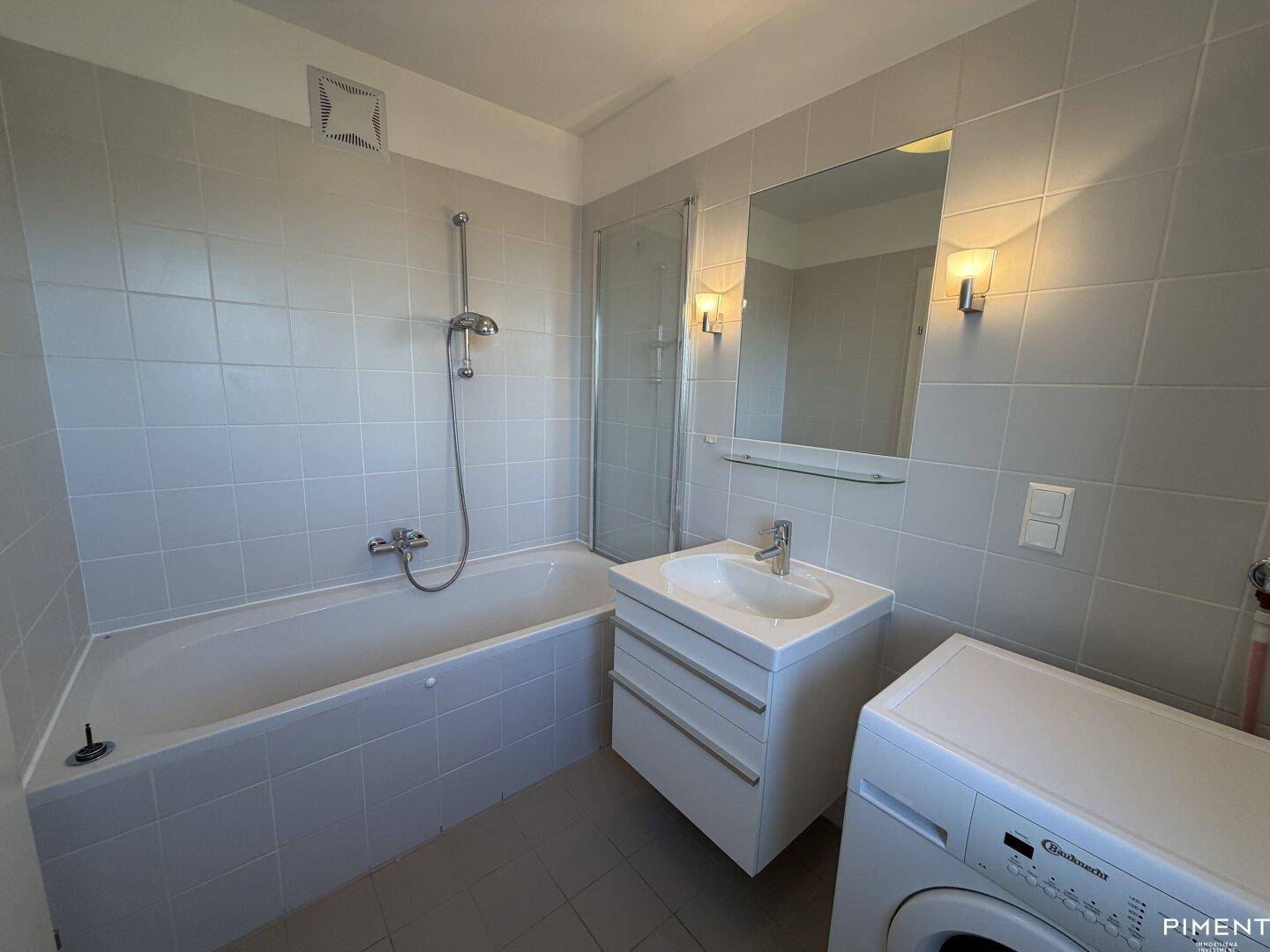 Gefliestes Badezimmer mit Badewanne, Duschfunktion, Waschbecken und Waschmaschine.
