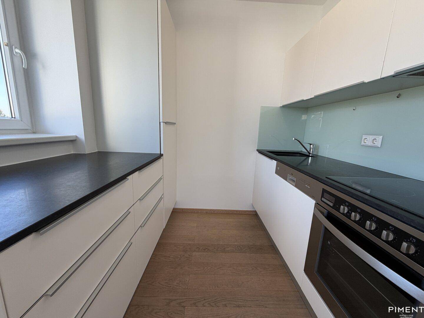 Moderne, schmale Küche mit weißen Schränken, dunkler Arbeitsplatte und integrierten Geräten.