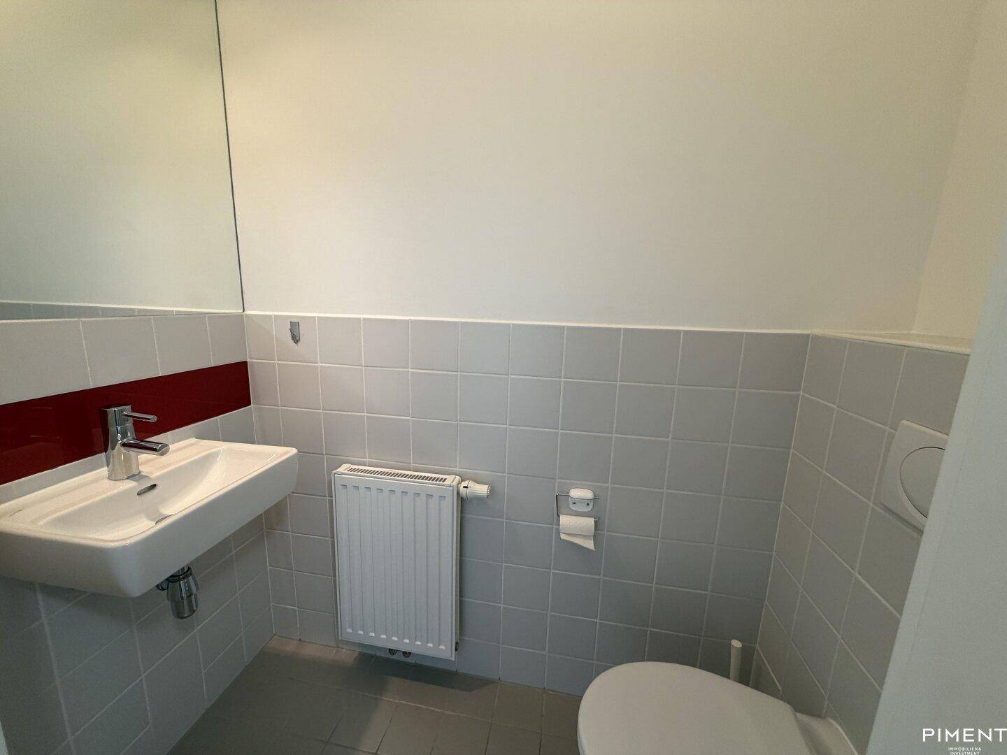 Kleines Gäste-WC mit Waschbecken, Toilette und hellgrauen Fliesen.