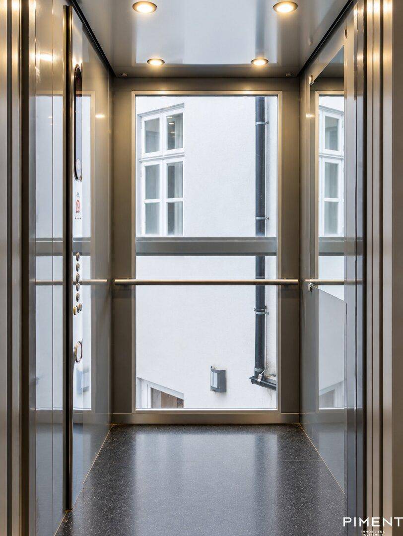Moderner Aufzug mit Glasfront und Blick auf den Innenhof des Gebäudes.