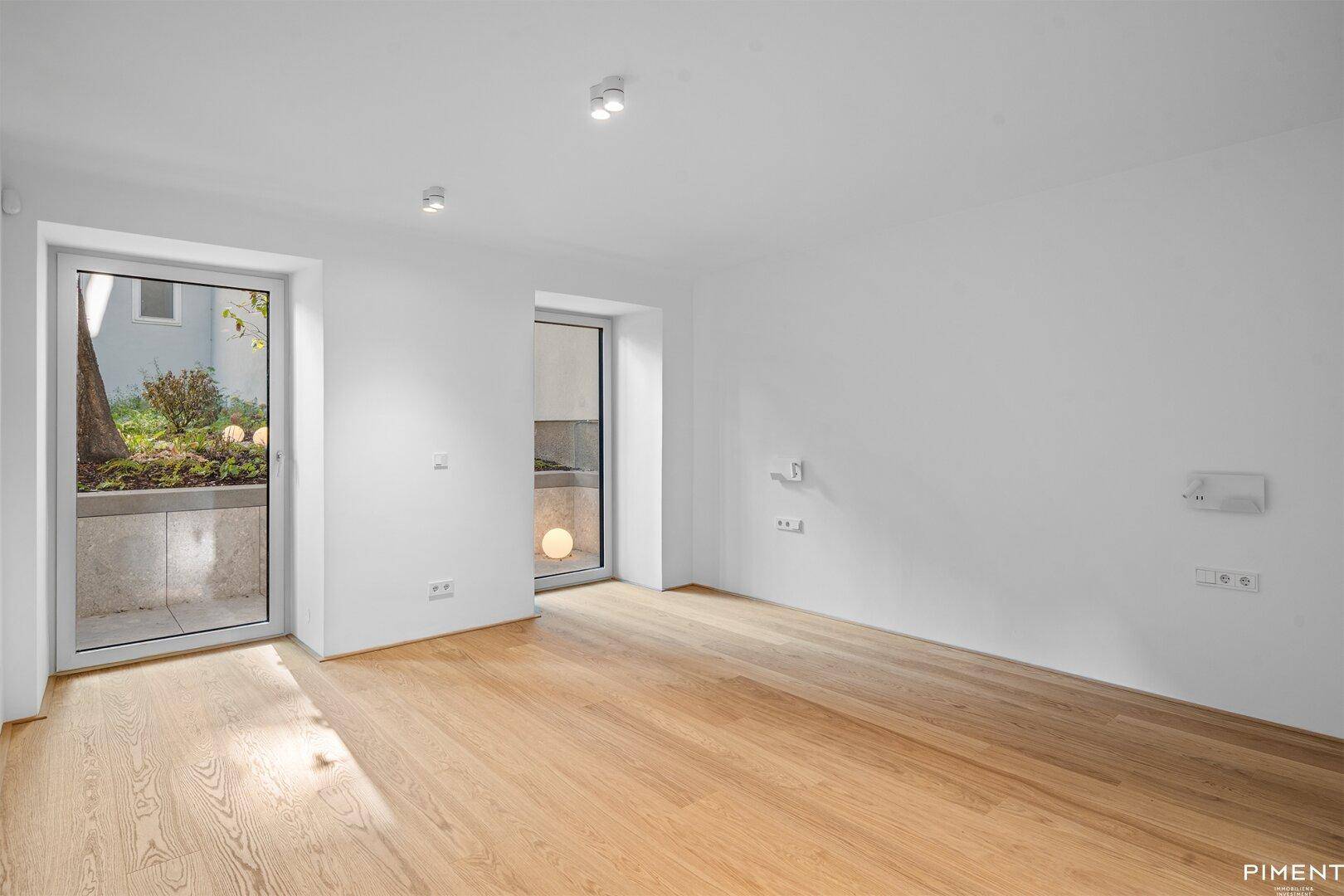 Lichtdurchfluteter Wohnraum mit Parkettboden und zwei großen Fenstertüren zum Außenbereich.