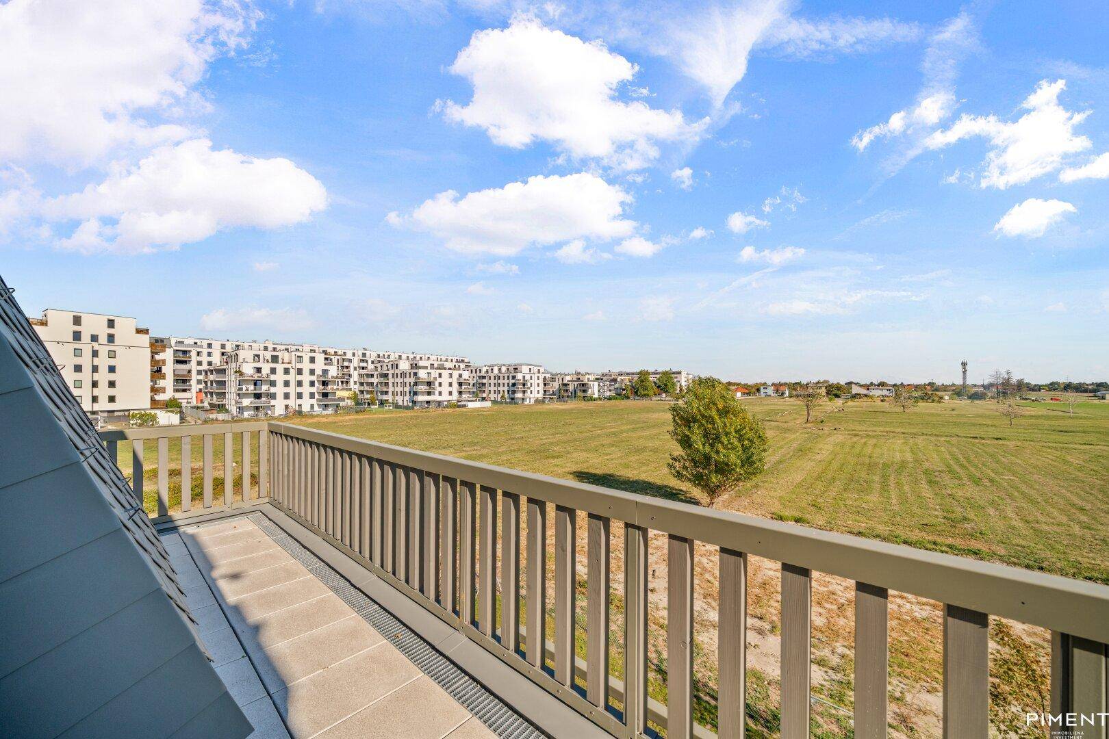 Großer Balkon mit weitem Blick über grüne Felder und moderne Wohngebäude.
