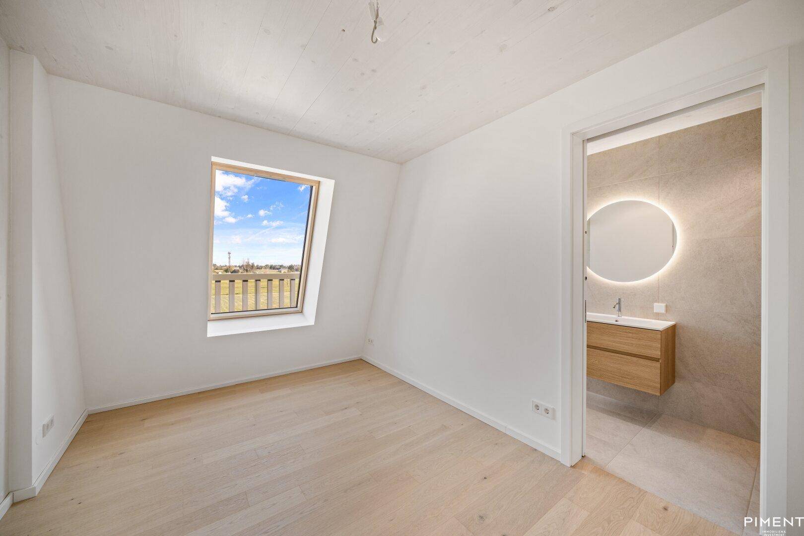 Helles Schlafzimmer mit Holzboden, Dachfenster und direktem Zugang zum modernen Bad.