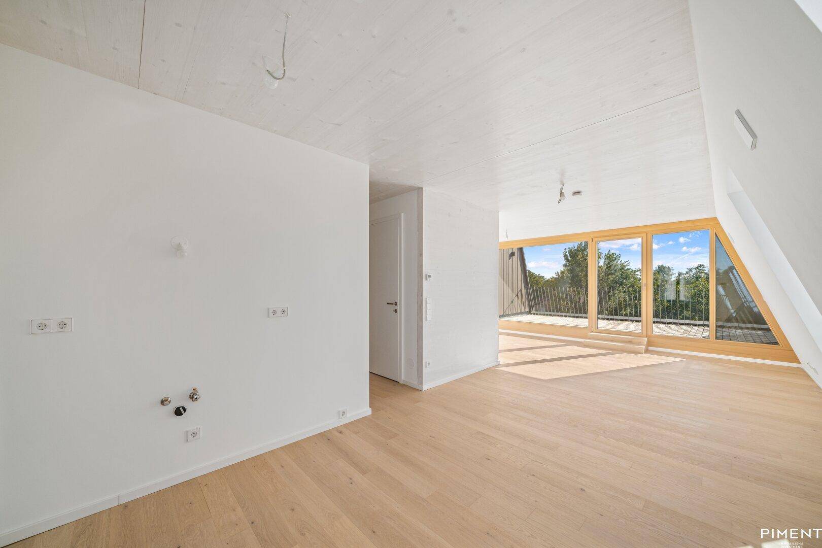 Lichtdurchfluteter Raum im Dachgeschoss mit Holzboden und Zugang zu einer Außenterrasse.