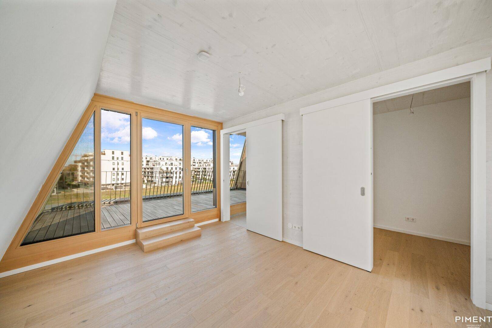 Heller Raum mit Holzboden, Schiebetüren und Zugang zu einem Balkon mit Stadtblick.