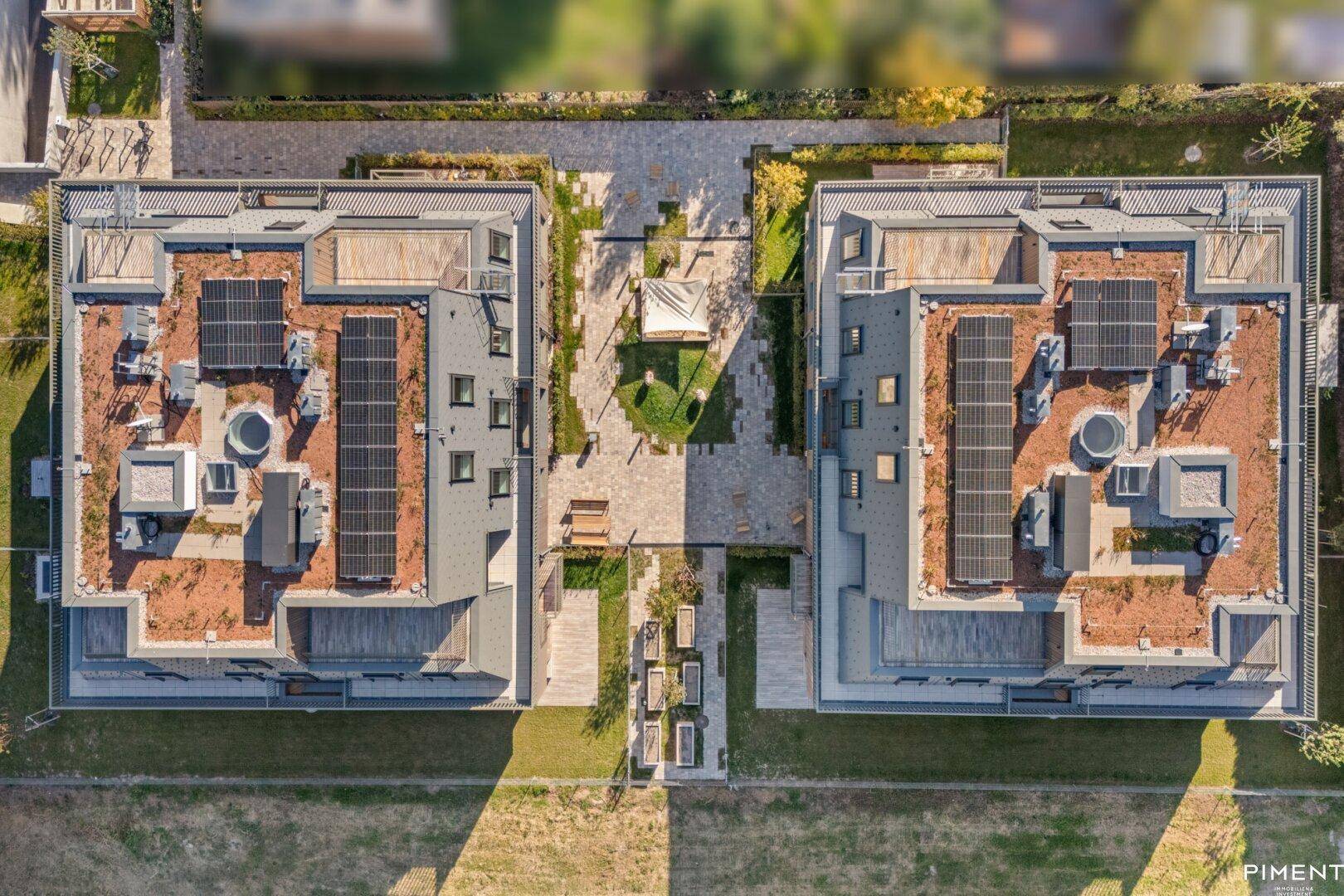 Vogelperspektive auf zwei moderne Wohngebäude mit Solaranlagen auf den Dächern und Innenhof.