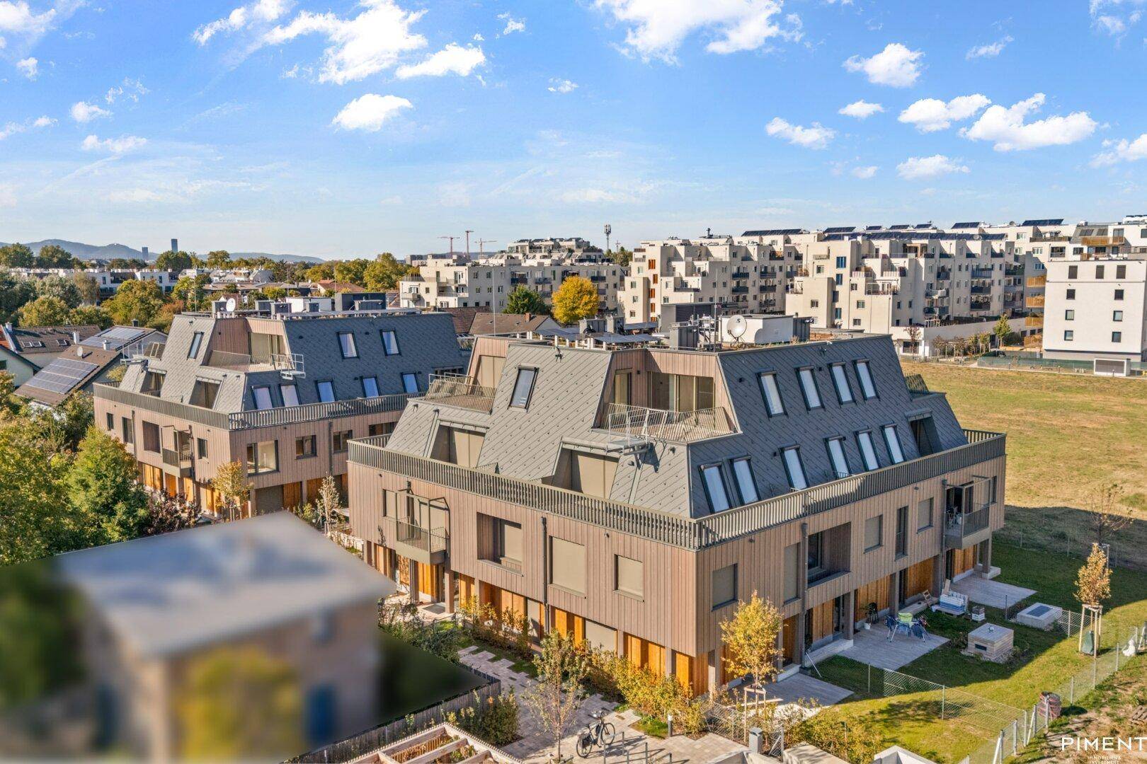 Moderne Wohnanlage mit mehreren Gebäuden und Mansarddächern in einer grünen Umgebung.