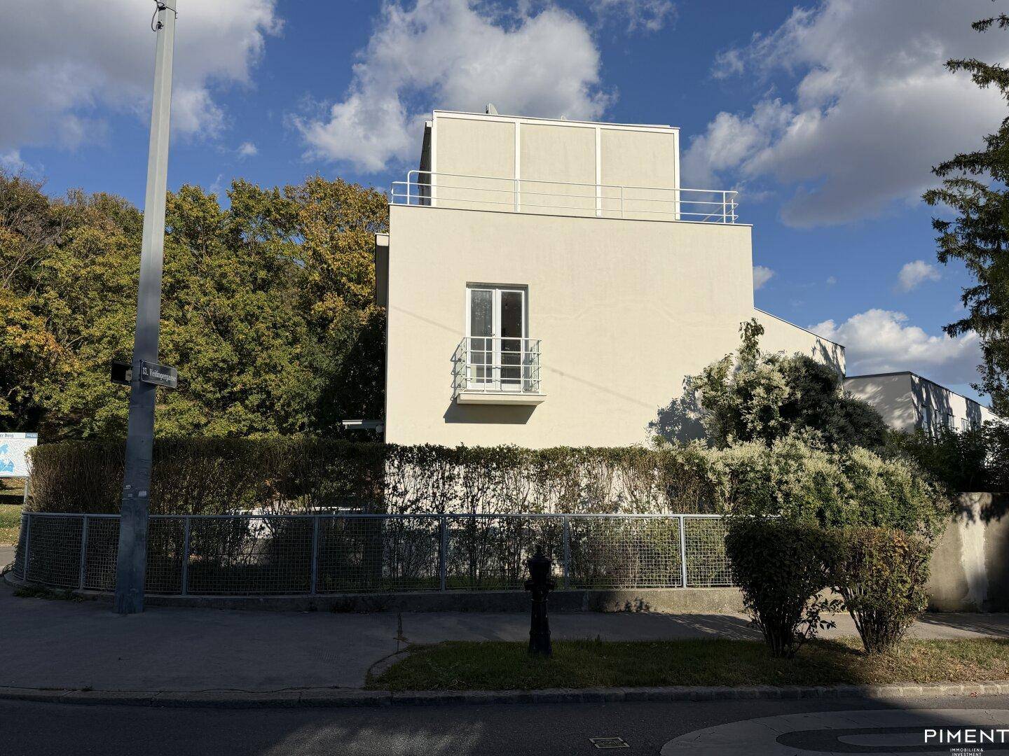 Außenansicht des modernen Hauses von der Straße mit gepflegter Hecke und Bäumen.