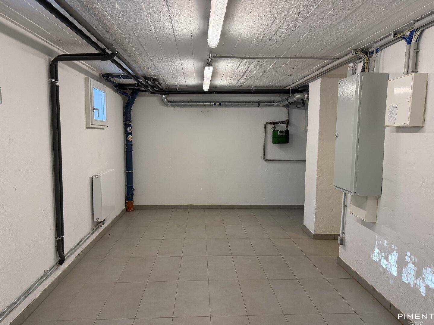 Kellerraum mit Fliesenboden, sichtbaren Leitungen und elektrischen Installationen.