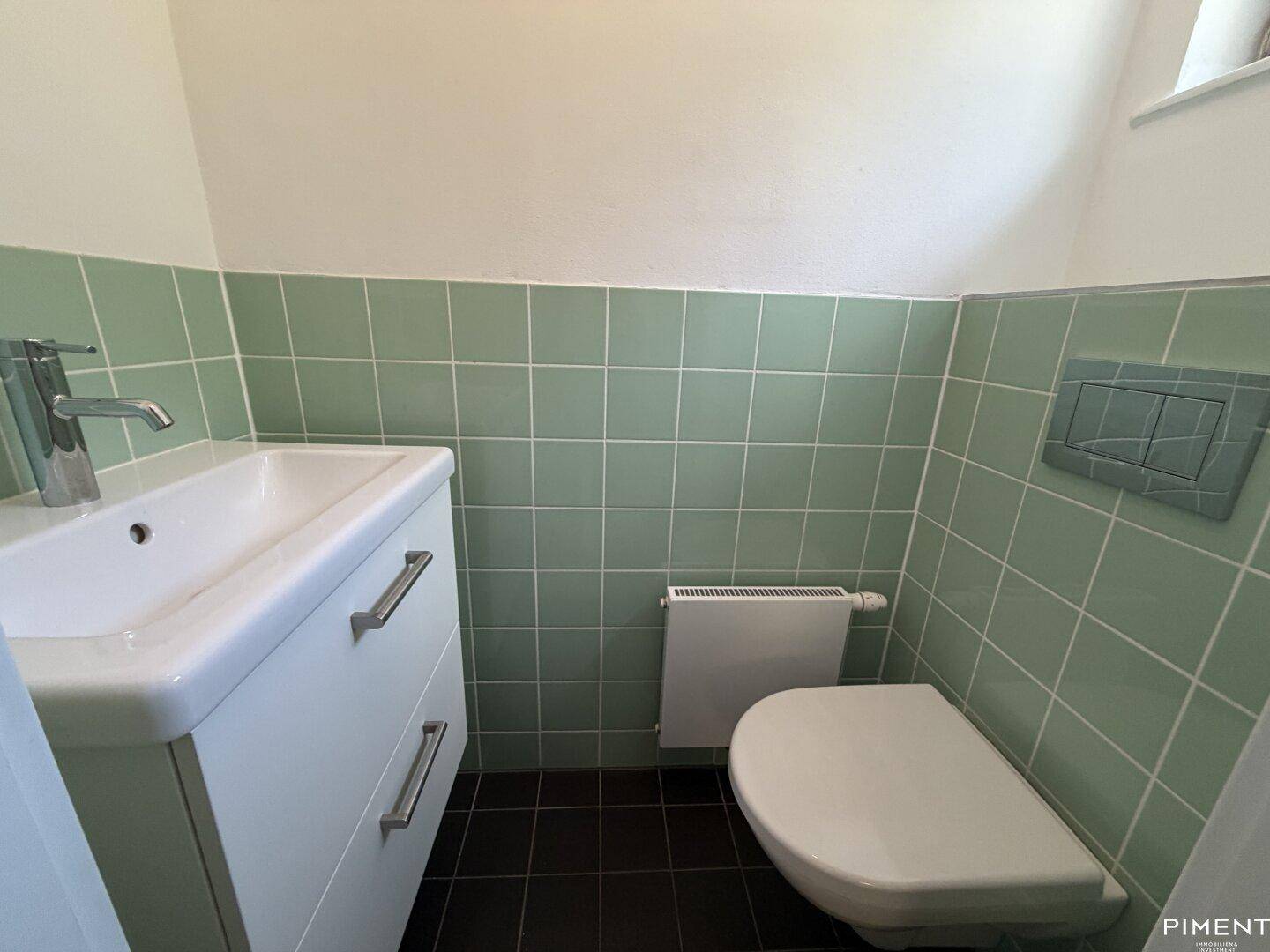 Gäste-WC mit hellgrünen Fliesen, einem Waschbecken mit Unterschrank und Wand-WC.