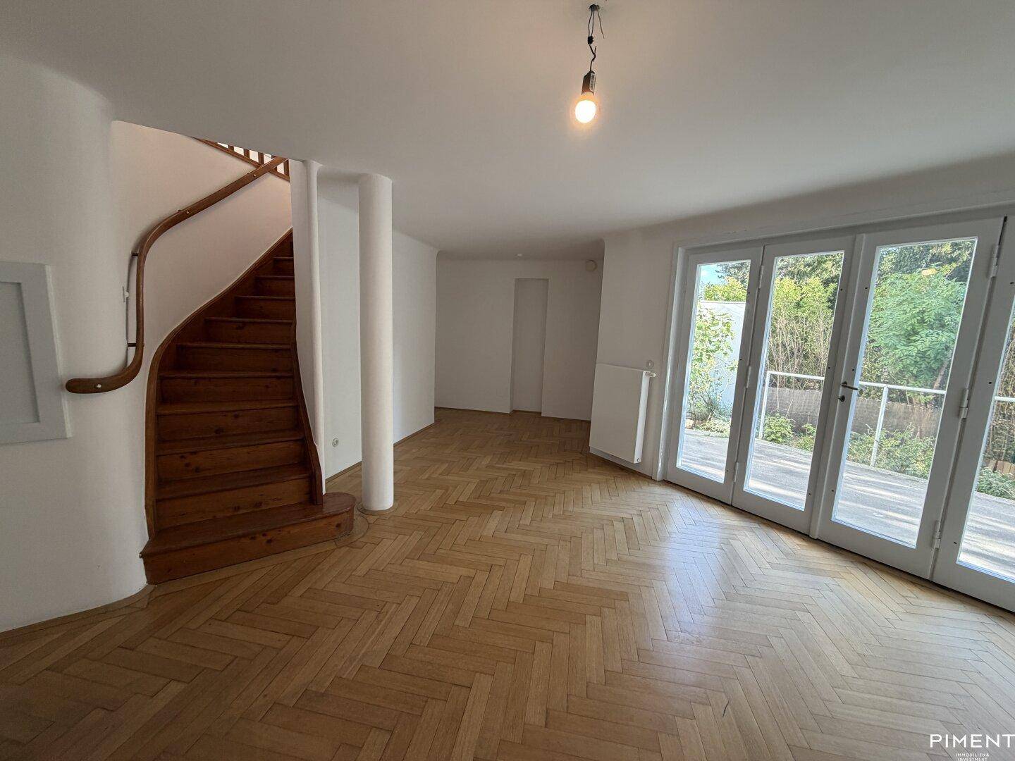 Helles Wohnzimmer mit Fischgrätparkett, einer Holztreppe und großen Fenstertüren zum Garten.