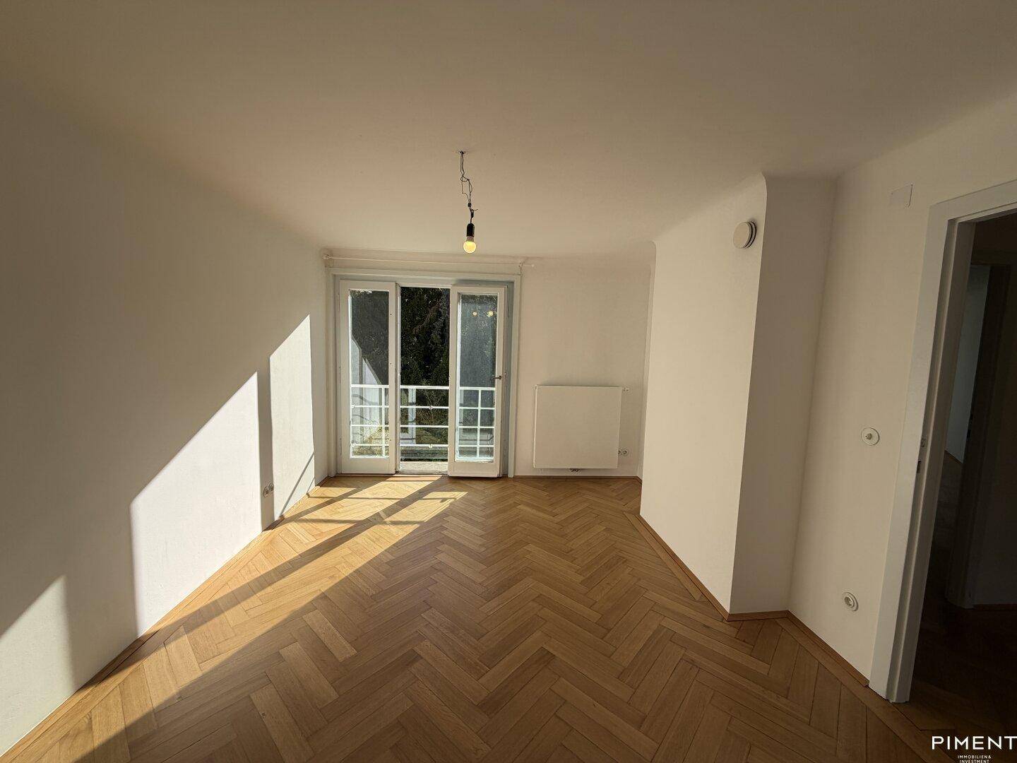 Sonnenverwöhntes Zimmer mit Fischgrätparkett und Zugang zu einem Balkon oder einer Terrasse.