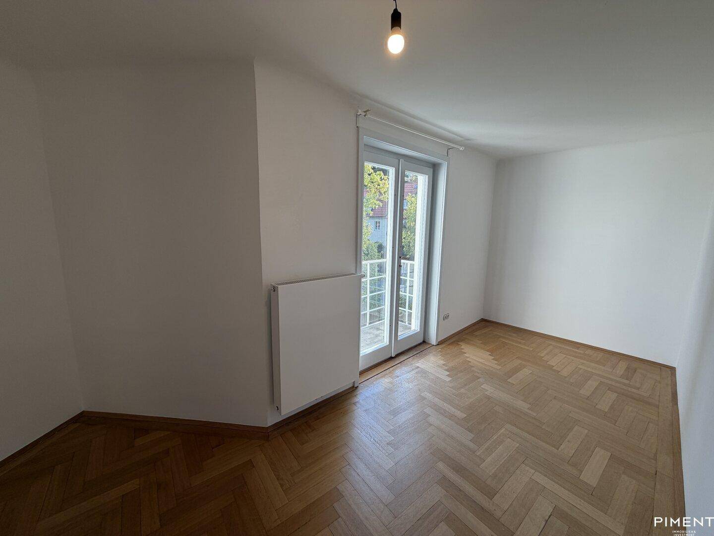 Helles Zimmer mit Fischgrätparkettboden und einem französischen Balkon, ideal als Schlafzimmer.