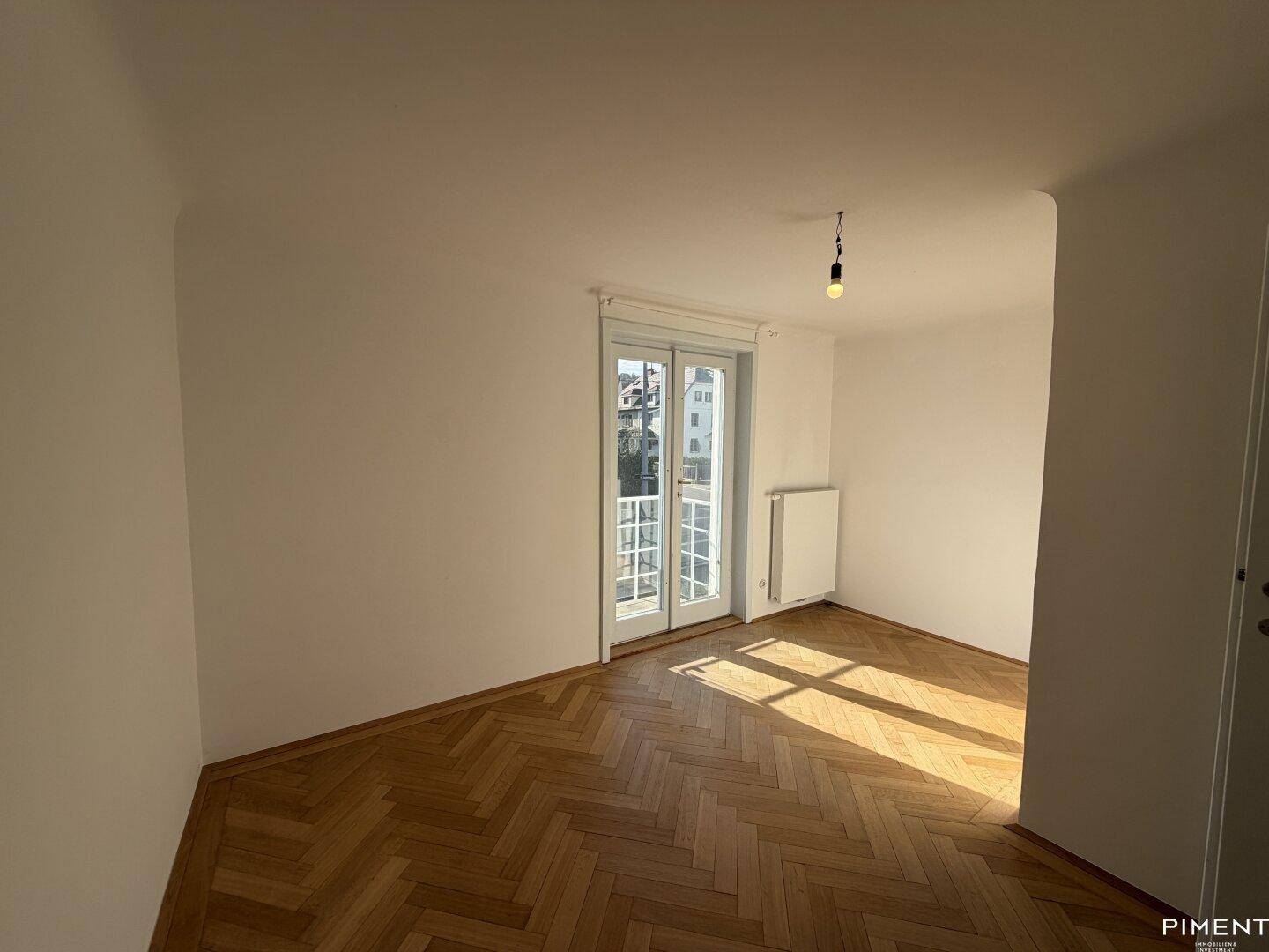 Sonniges Schlafzimmer mit klassischem Fischgrätparkett und einem französischen Balkon.