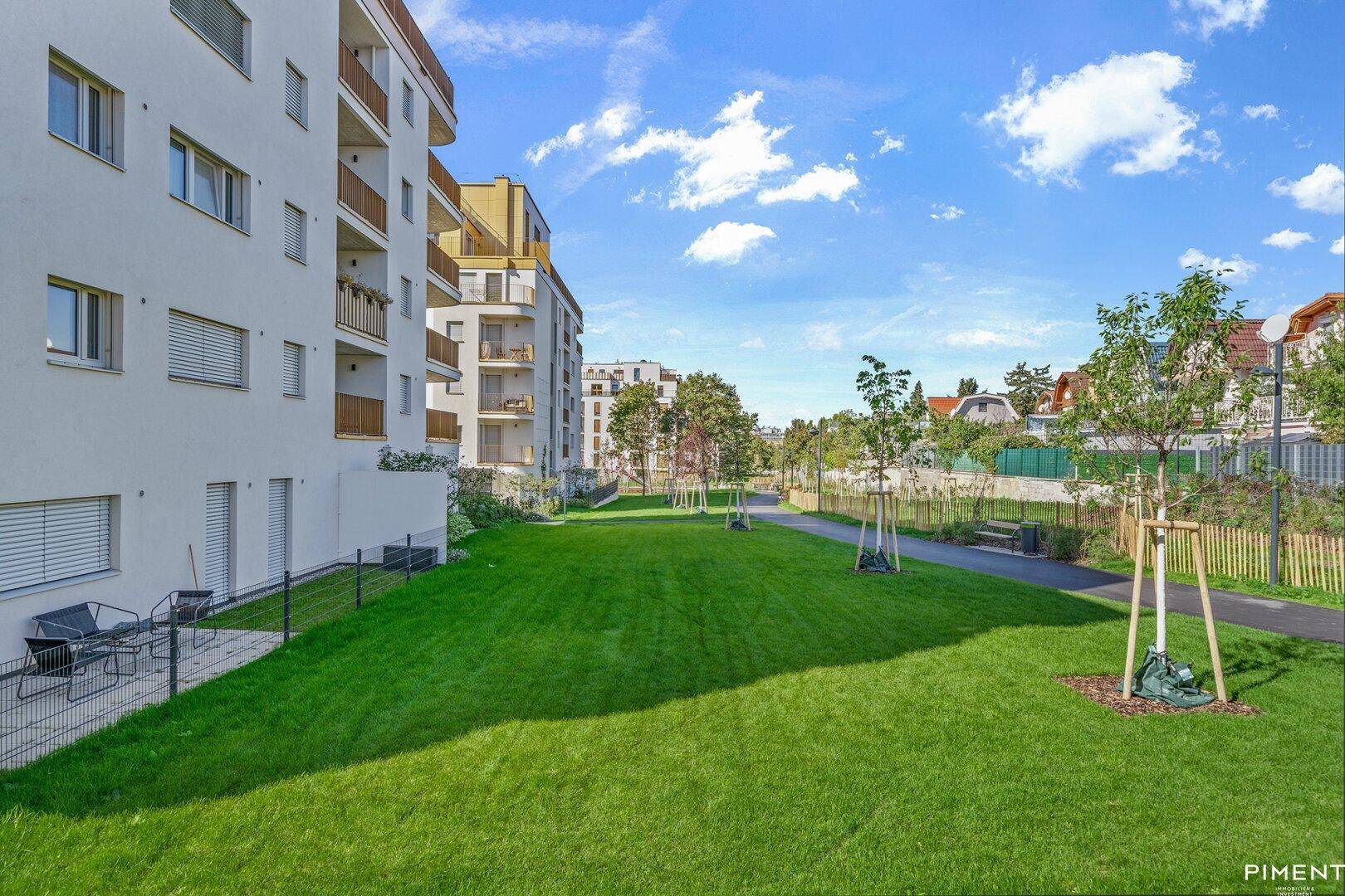 Moderne Wohngebäude mit Balkonen und privaten Gärten im Erdgeschoss, umgeben von Grünflächen.