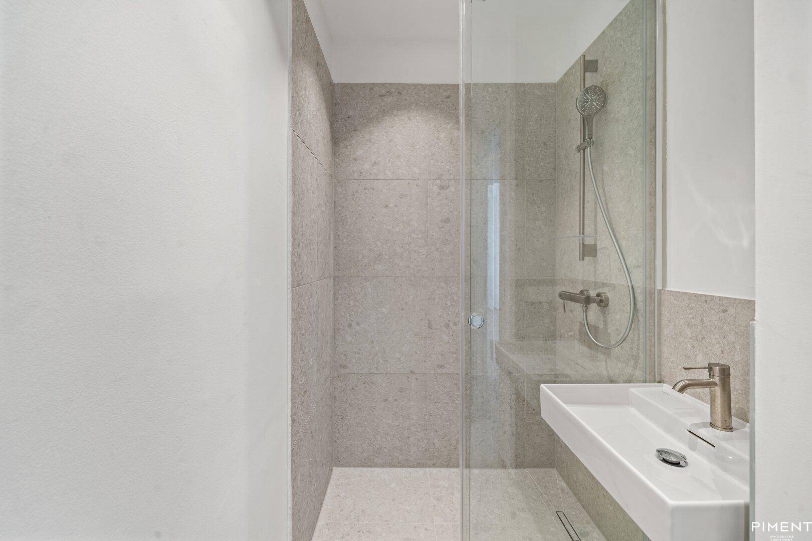 Elegantes Badezimmer mit grauen Fliesen, moderner Dusche und stilvollem Waschbecken.